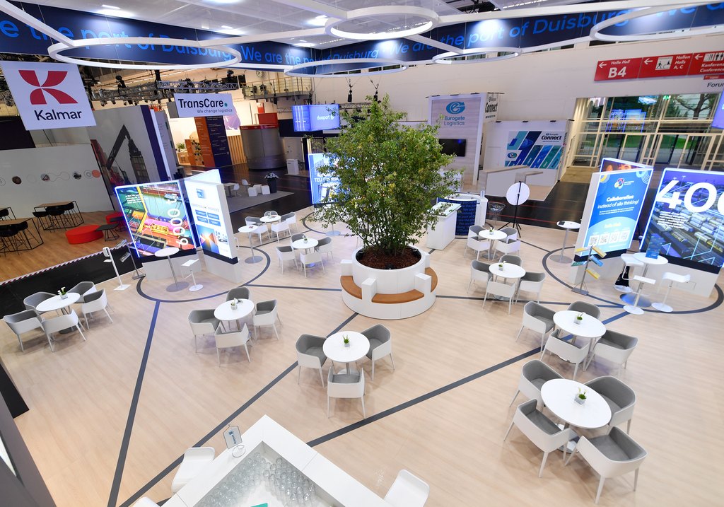 Moderner Logistik-Messestand mit Sitzgruppen und digitalen Displays